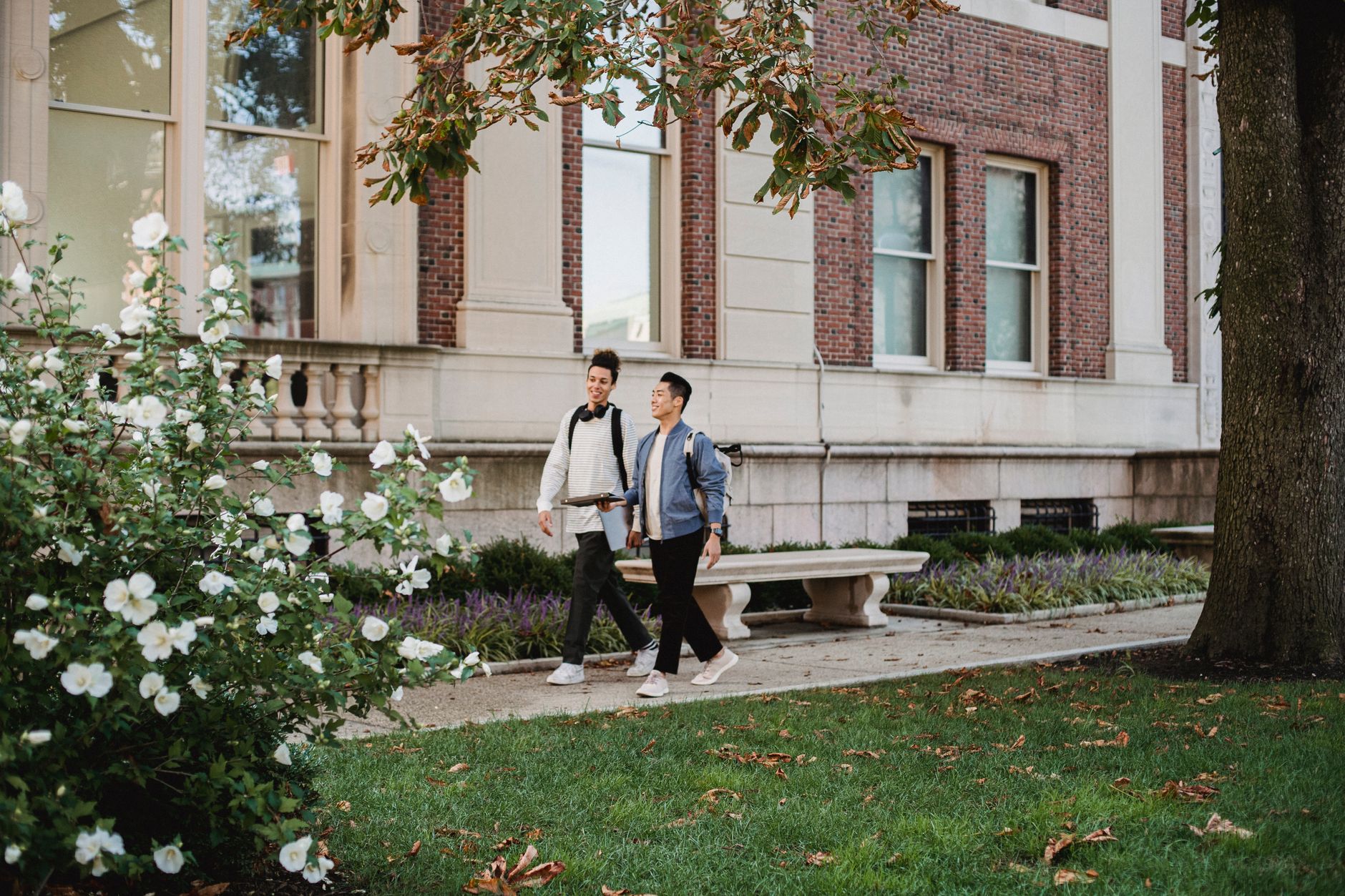 Full body of smiling multiracial friends strolling together along pavement while talking to each other in park