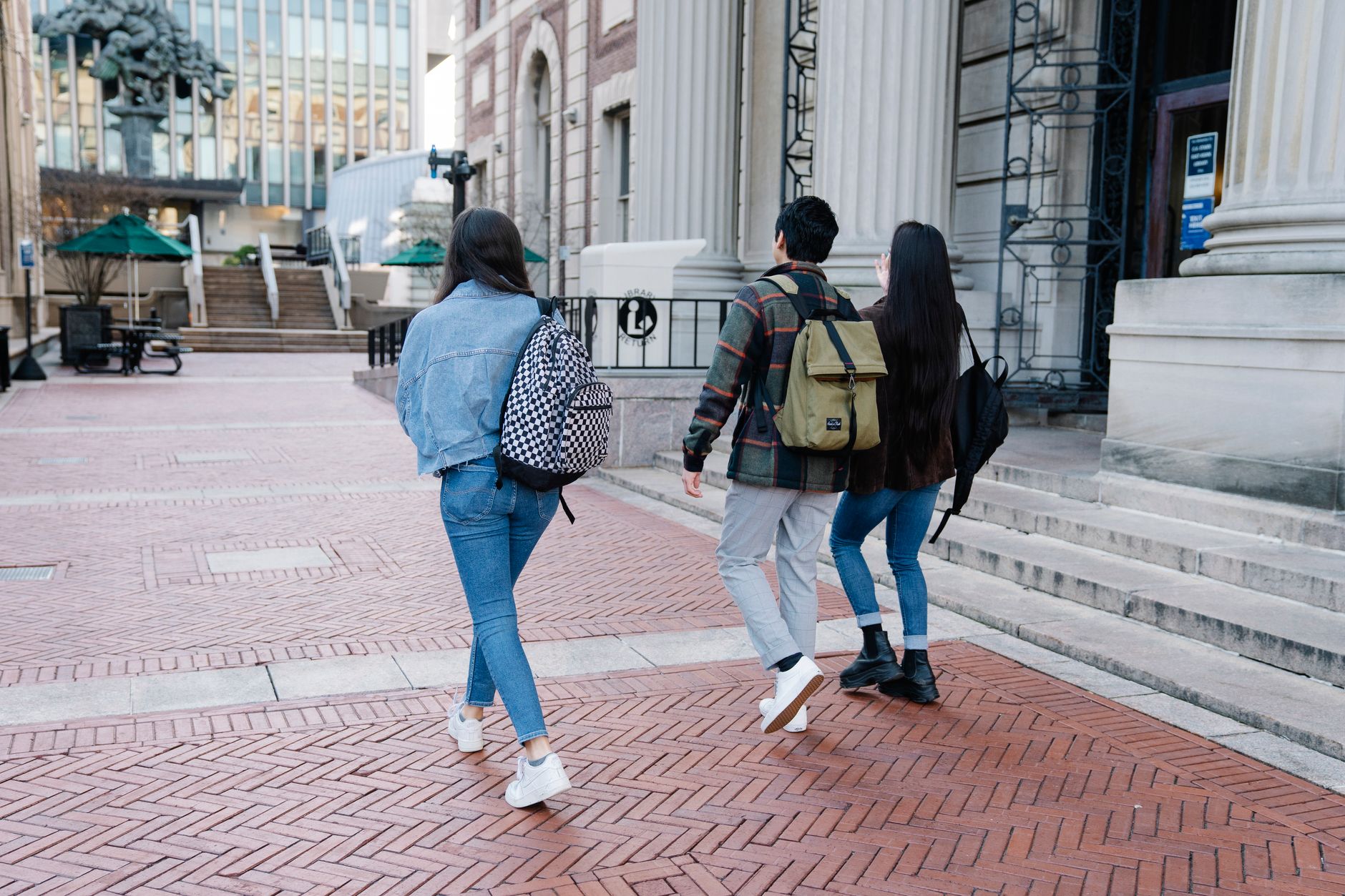 A group of young students walk along a university campus pathway, carrying backpacks.