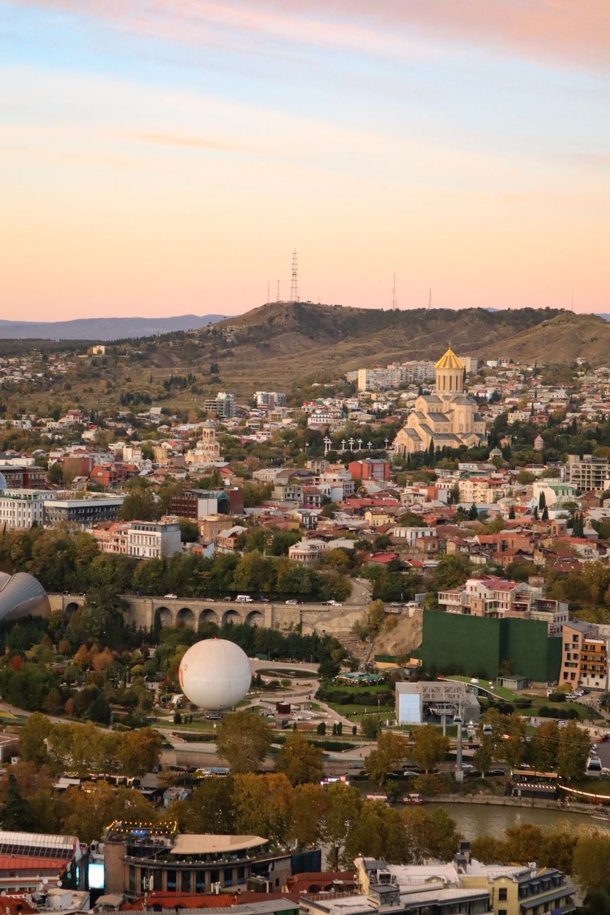 Aerial view of Tbilisi showcasing iconic landmarks and vibrant cityscape under a clear sky.