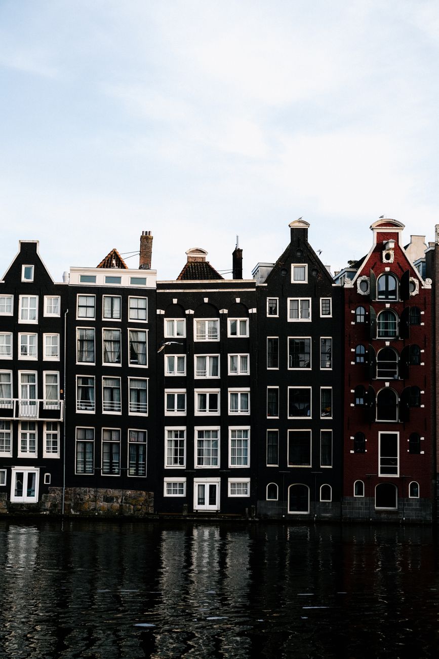 Exterior of narrow multicolored apartment houses without balconies overseeing canal with modern boats moored near entrances