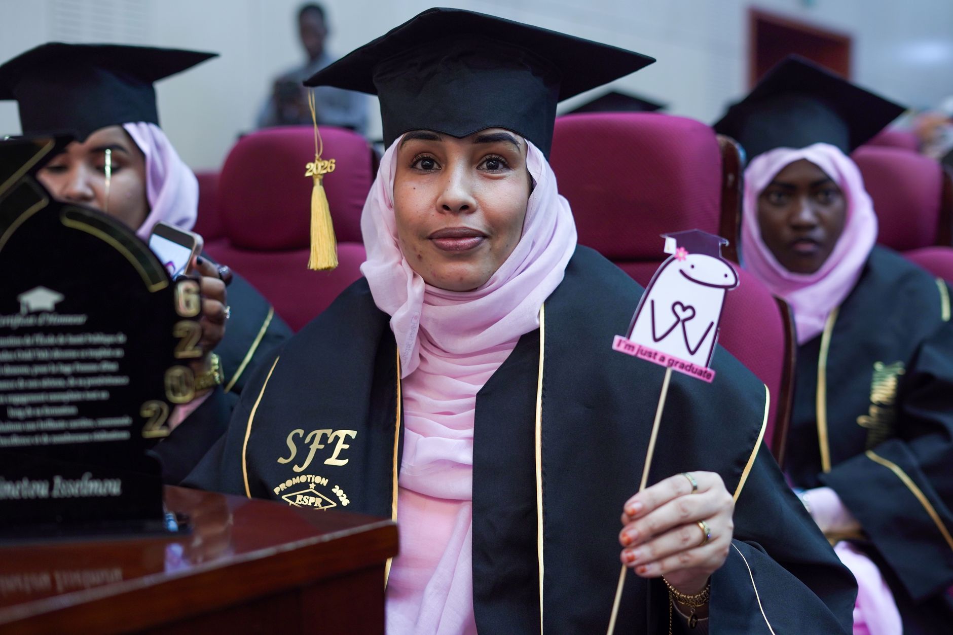 Graduates in hijabs celebrating at a ceremony, wearing caps and gowns.