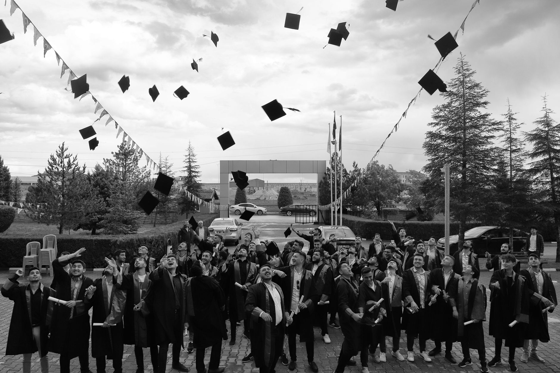 A group of university graduates in gowns and caps celebrate outdoors by tossing their caps into the air.