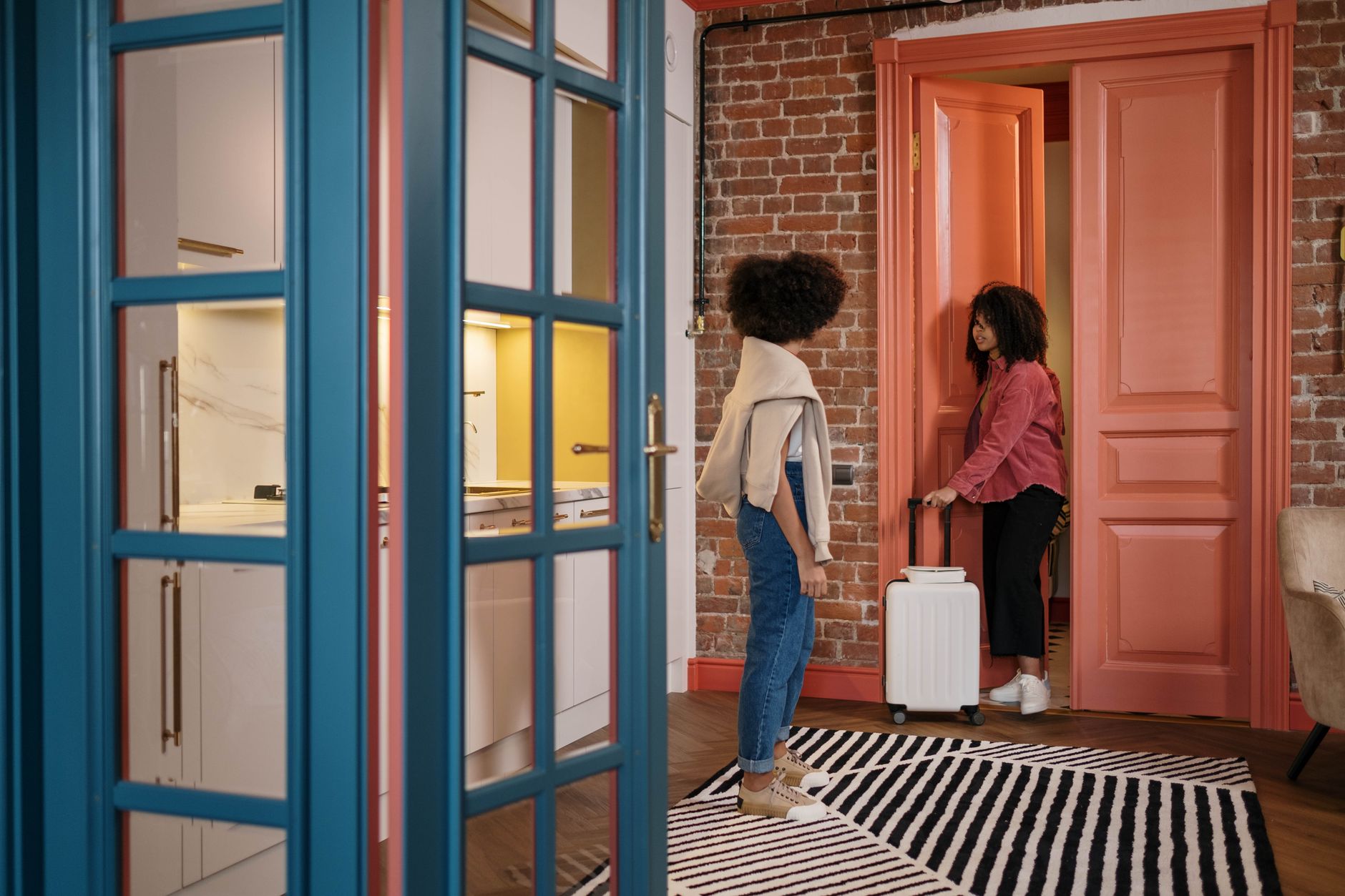 Two women with luggage in a stylish apartment hallway, getting ready to travel.