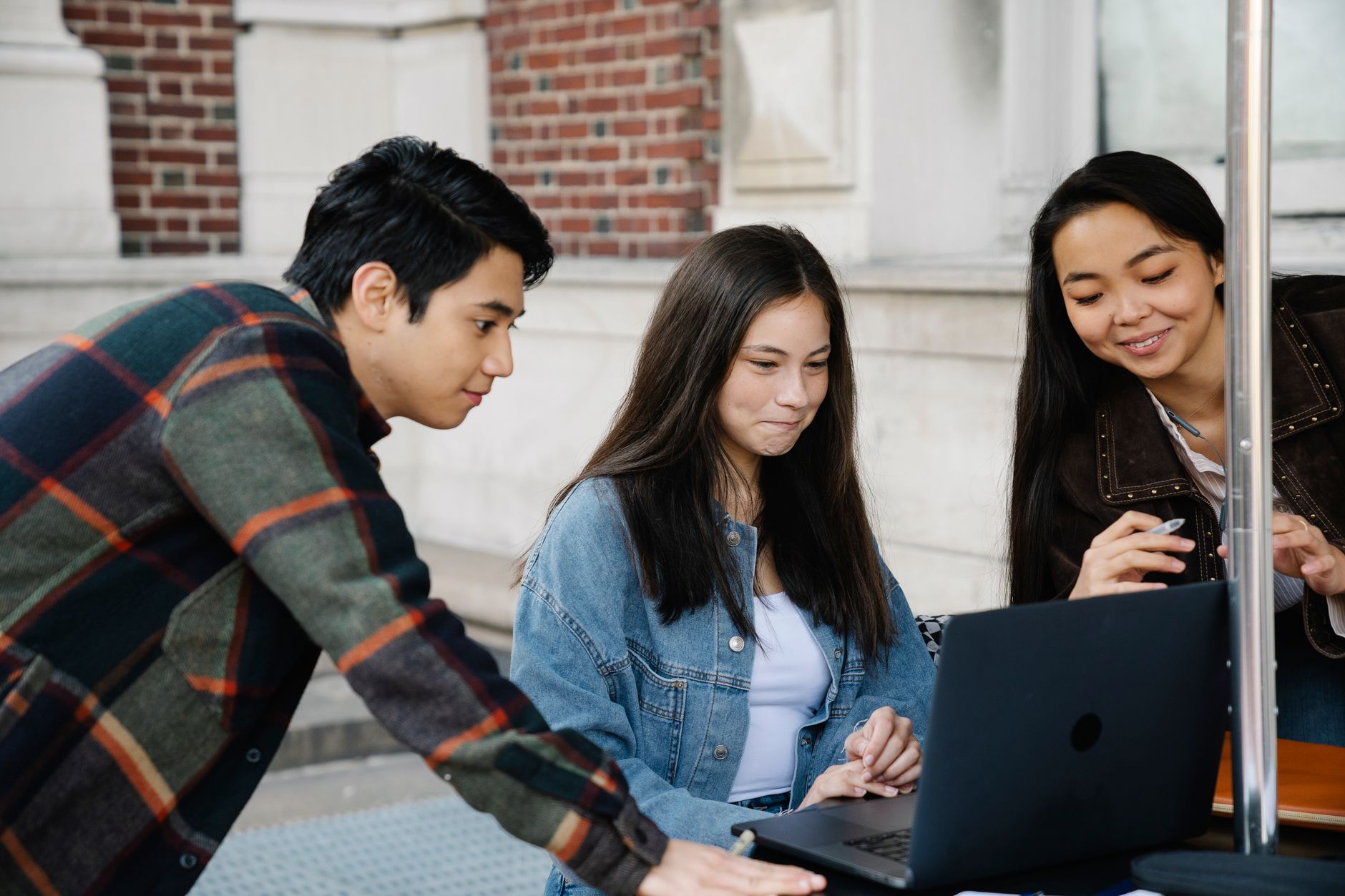 Diverse group of college students studying outdoors with a laptop, fostering collaboration.
