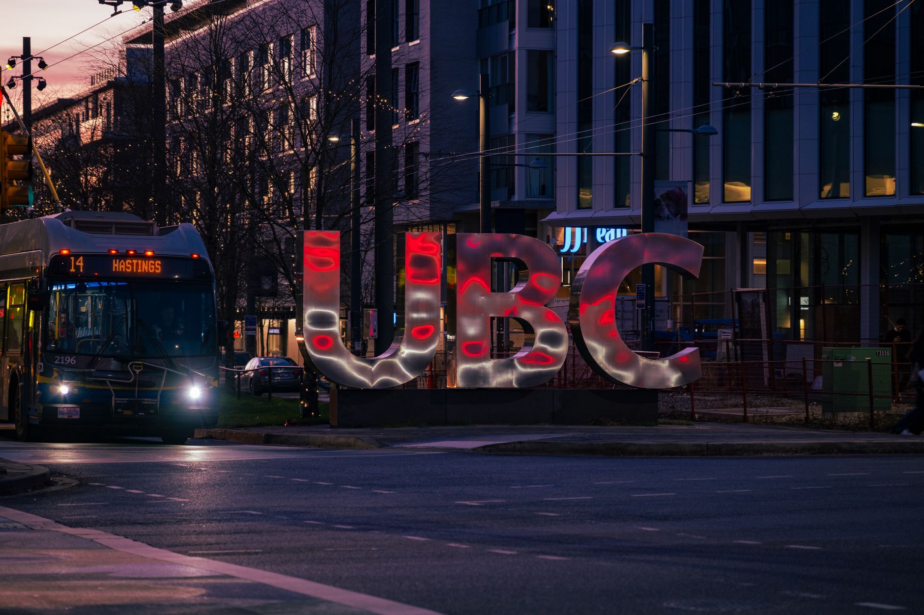 Evening scene of UBC sign illuminated with city bus at University Endowment Lands in Vancouver, BC.